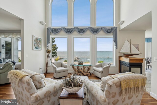 living room featuring a high ceiling, a multi sided fireplace, a water view, and wood-type flooring