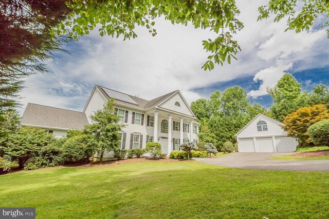 view of front of house with a garage, solar panels, a front lawn, and an outdoor structure