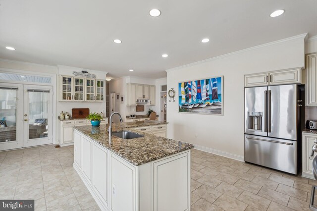 kitchen featuring high end refrigerator, sink, dark stone countertops, a kitchen island with sink, and light tile patterned floors