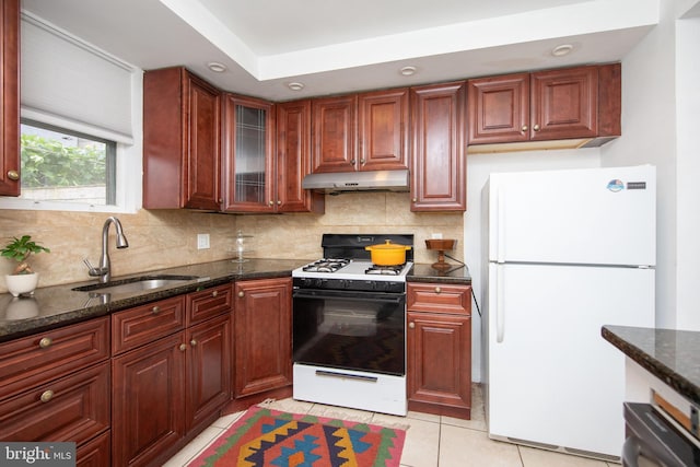 kitchen with sink, dark stone countertops, white fridge, light tile patterned floors, and gas stove