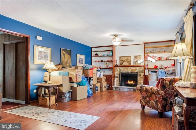 living room featuring ceiling fan, hardwood / wood-style floors, and a stone fireplace