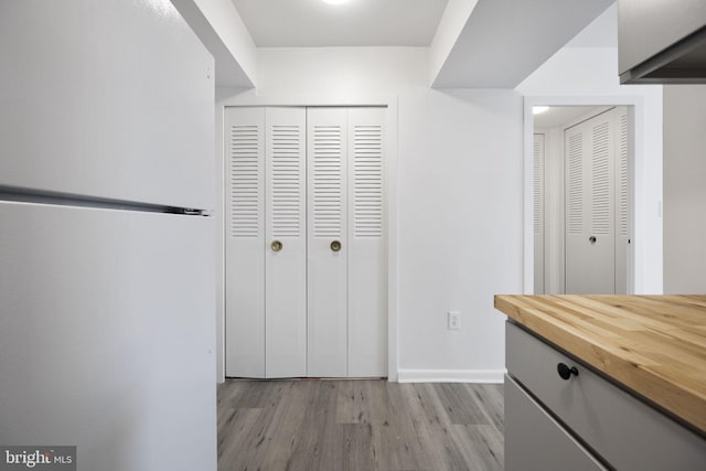 interior space featuring baseboards, light wood-type flooring, freestanding refrigerator, and wooden counters