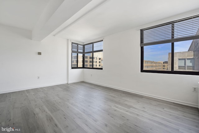 unfurnished room with beamed ceiling, wood finished floors, and baseboards