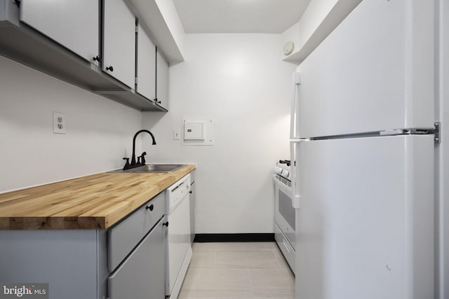 kitchen featuring white appliances, light tile patterned floors, baseboards, gray cabinetry, and a sink