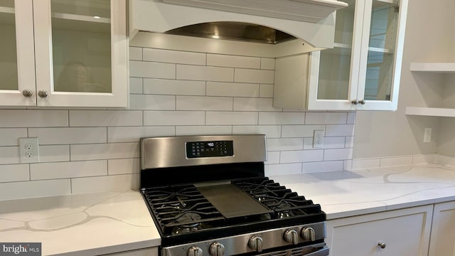 kitchen featuring stainless steel range with gas stovetop, white cabinetry, light stone counters, backsplash, and range hood