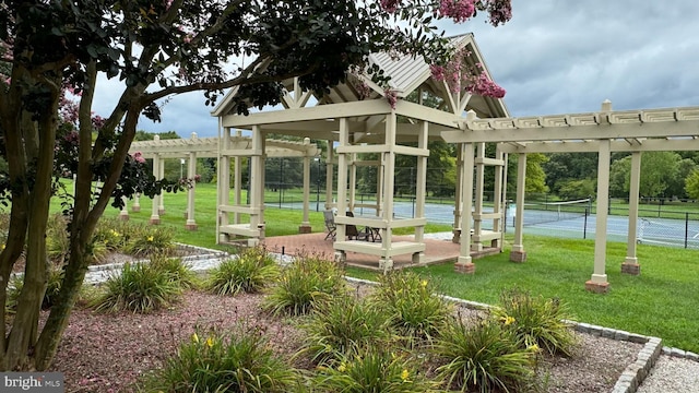 view of community featuring tennis court, a yard, and a pergola