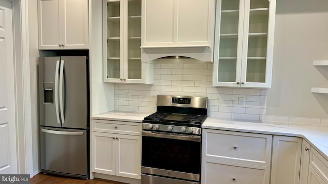 kitchen with tasteful backsplash, light stone counters, white cabinetry, appliances with stainless steel finishes, and dark hardwood / wood-style flooring