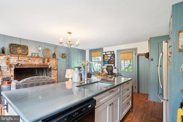 kitchen with sink, a brick fireplace, a kitchen island with sink, dark wood-type flooring, and a notable chandelier