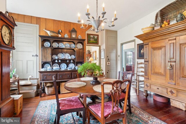 dining area featuring a notable chandelier, wooden walls, and dark hardwood / wood-style flooring