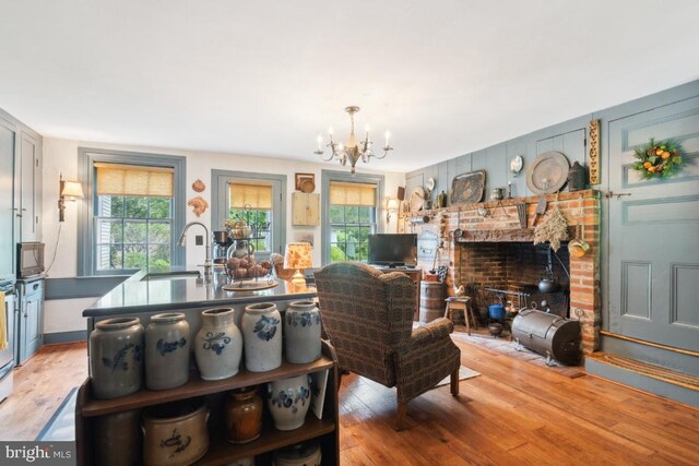 living room featuring a notable chandelier, light hardwood / wood-style floors, sink, and a brick fireplace