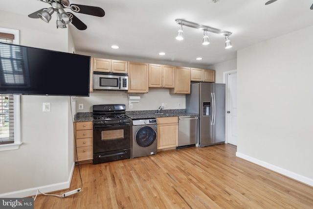 kitchen featuring light wood finished floors, stainless steel appliances, dark countertops, light brown cabinetry, and washer / dryer