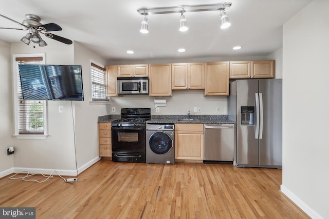 kitchen with light brown cabinets, appliances with stainless steel finishes, light wood-type flooring, washer / clothes dryer, and dark countertops