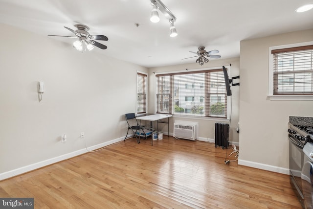 interior space with light wood-style flooring, black gas range oven, radiator heating unit, a wall mounted air conditioner, and baseboards