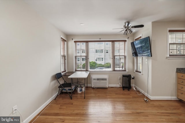 sitting room featuring light wood-type flooring, radiator, a wall mounted air conditioner, and baseboards