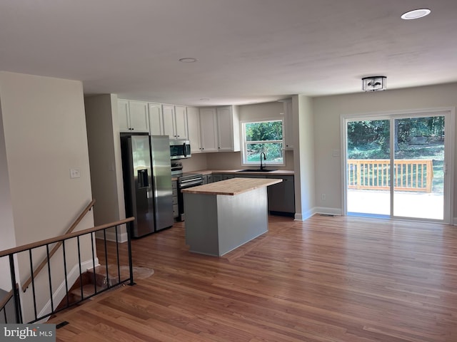 kitchen featuring light wood finished floors, a center island, stainless steel appliances, white cabinetry, and a sink