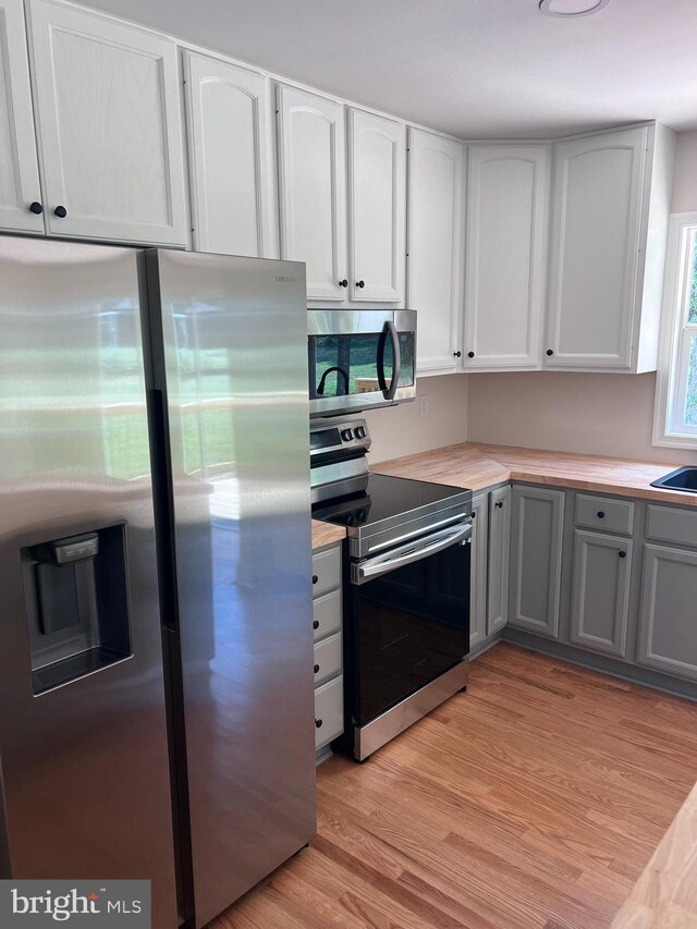 kitchen with appliances with stainless steel finishes, white cabinets, gray cabinetry, and light wood-type flooring