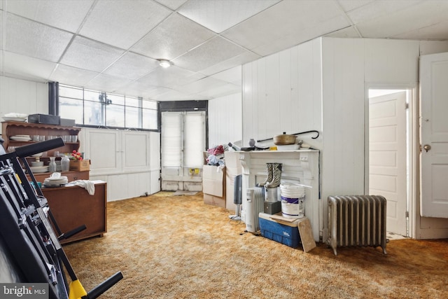 basement featuring carpet, radiator heating unit, and a paneled ceiling