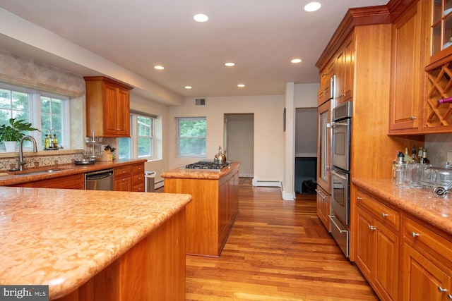 kitchen with appliances with stainless steel finishes, light wood-type flooring, a kitchen island, sink, and backsplash