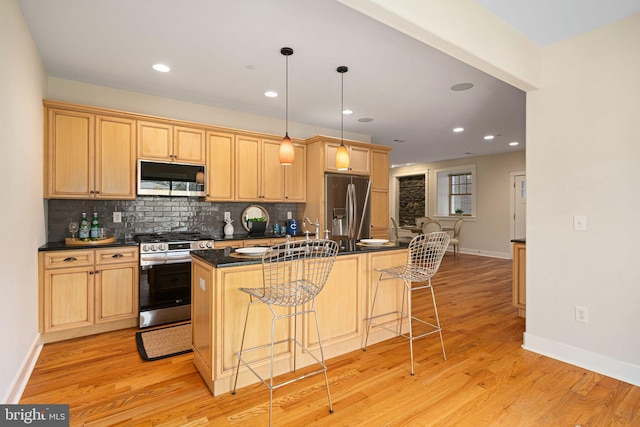 kitchen with light hardwood / wood-style floors, appliances with stainless steel finishes, a kitchen bar, decorative light fixtures, and a center island with sink