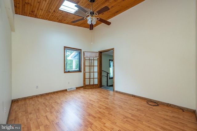 empty room featuring a skylight, light wood-type flooring, high vaulted ceiling, ceiling fan, and wooden ceiling