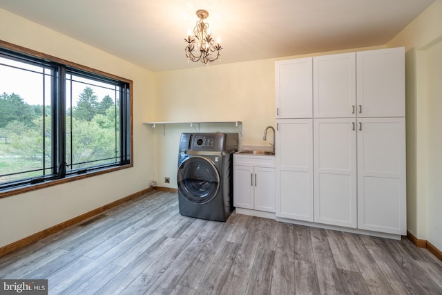 clothes washing area with light hardwood / wood-style flooring, cabinets, sink, a notable chandelier, and washer / clothes dryer