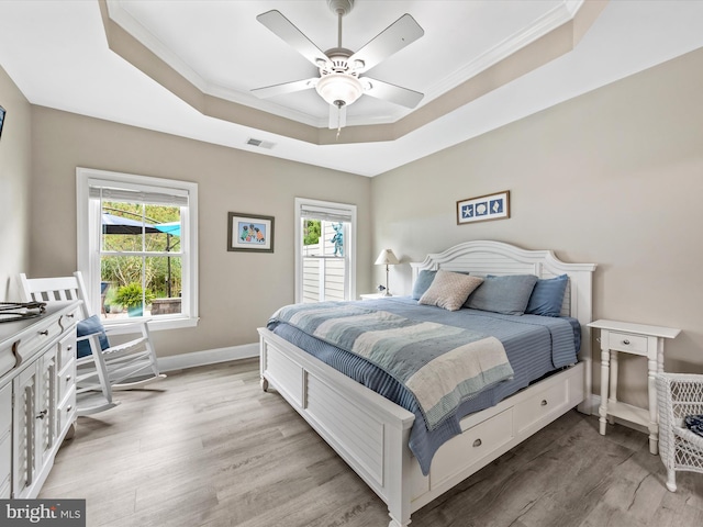 bedroom with light hardwood / wood-style floors, multiple windows, a tray ceiling, and ceiling fan