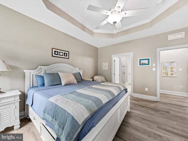 bedroom with light hardwood / wood-style flooring, ceiling fan, ornamental molding, connected bathroom, and a tray ceiling