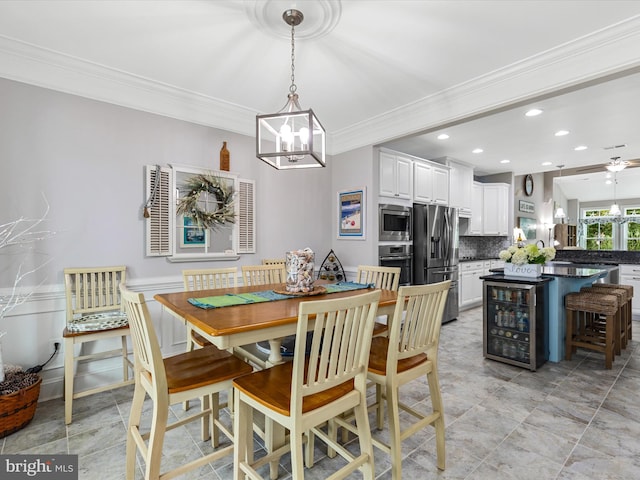 dining area featuring ceiling fan with notable chandelier, crown molding, and beverage cooler