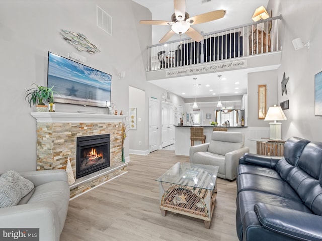 living room with ceiling fan, a fireplace, light hardwood / wood-style floors, and a high ceiling