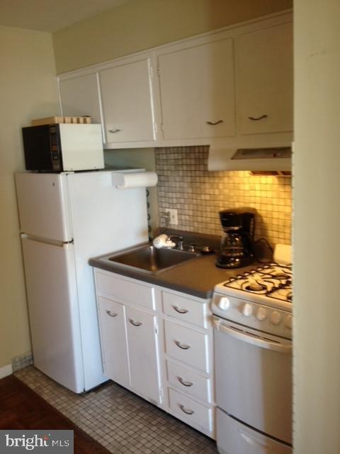 kitchen with white cabinetry, tile patterned flooring, sink, wall chimney range hood, and white appliances