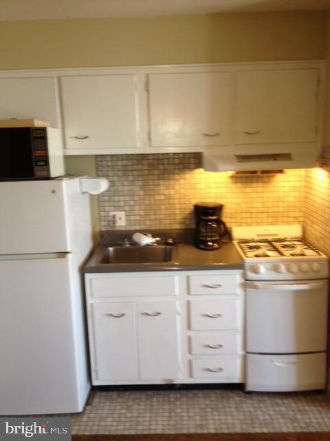 kitchen featuring backsplash, sink, gas range oven, and white refrigerator