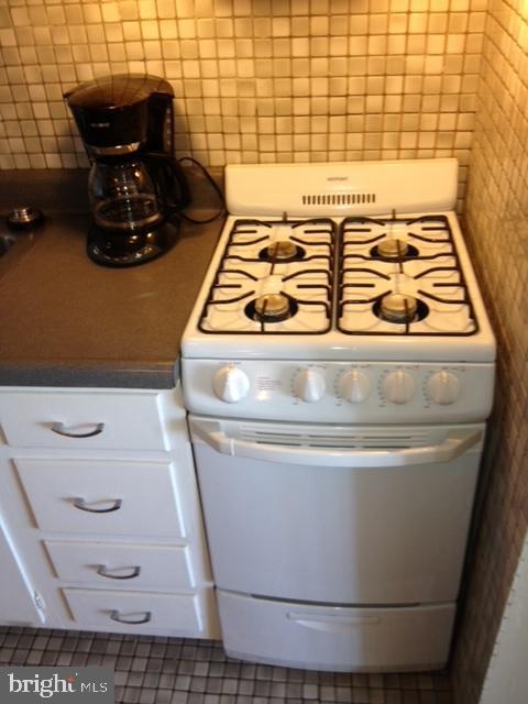 interior space featuring white stove, tile walls, tile patterned flooring, and white cabinetry