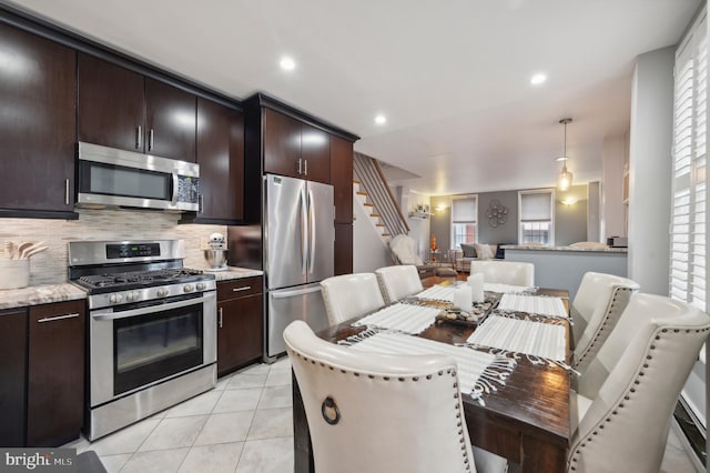 kitchen featuring light tile patterned floors, appliances with stainless steel finishes, hanging light fixtures, tasteful backsplash, and light stone counters