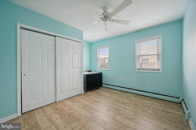 unfurnished bedroom with baseboard heating, light wood-type flooring, ceiling fan, and a closet