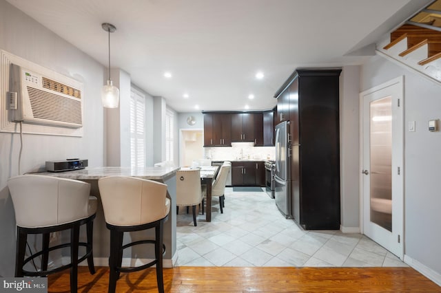 kitchen with an AC wall unit, stainless steel fridge, decorative backsplash, dark brown cabinetry, and kitchen peninsula