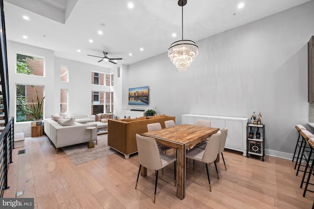 dining room featuring ceiling fan with notable chandelier, a high ceiling, and light hardwood / wood-style floors