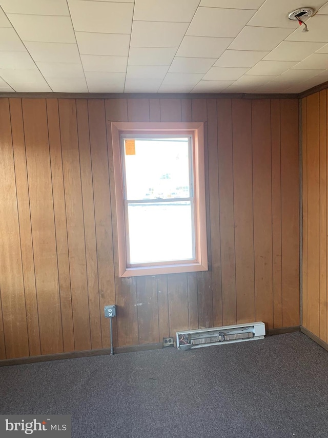 carpeted empty room with wood walls and a baseboard radiator