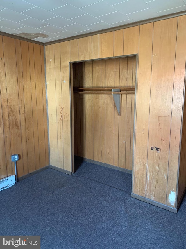 unfurnished bedroom featuring carpet flooring, a closet, and wooden walls