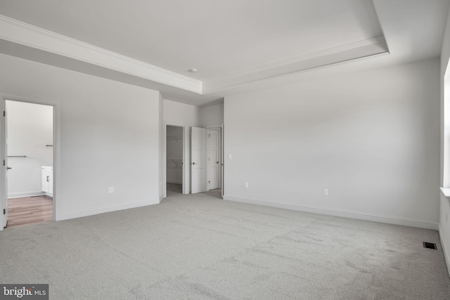 unfurnished bedroom featuring a tray ceiling, light colored carpet, ensuite bathroom, and a spacious closet