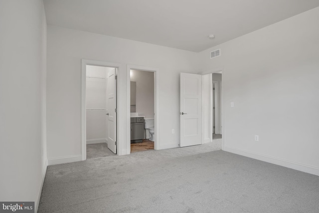 unfurnished bedroom with light carpet, connected bathroom, a walk in closet, and a closet