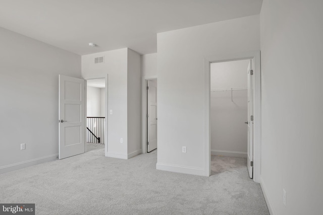 unfurnished bedroom with a walk in closet, light colored carpet, and a closet