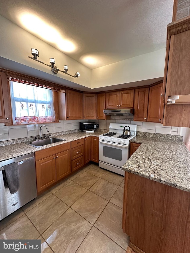 kitchen with brown cabinets, gas range gas stove, stainless steel dishwasher, under cabinet range hood, and a sink