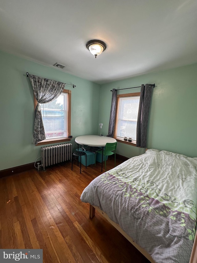 bedroom featuring radiator, multiple windows, visible vents, and wood finished floors