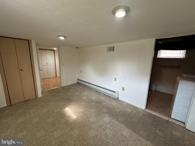 unfurnished bedroom with a textured ceiling, carpet, baseboard heating, and washer / dryer