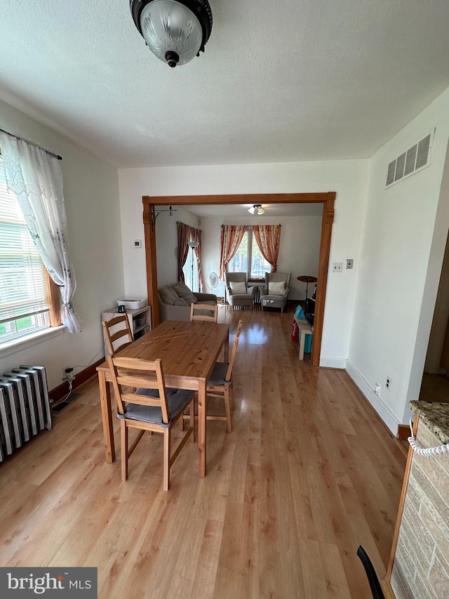 dining area with visible vents, radiator heating unit, light wood-style floors, a textured ceiling, and baseboards