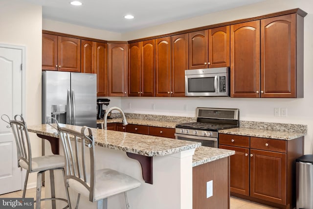 kitchen featuring a kitchen island with sink, stainless steel appliances, and light stone countertops