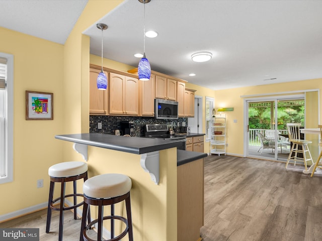 kitchen featuring a breakfast bar, decorative light fixtures, decorative backsplash, kitchen peninsula, and stainless steel appliances