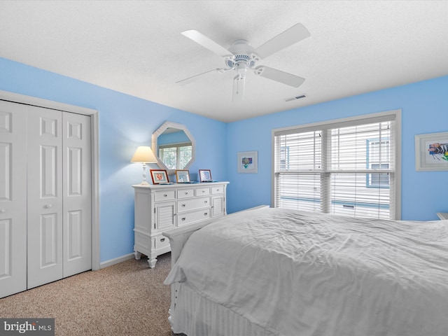 bedroom with ceiling fan, a closet, a textured ceiling, and light colored carpet