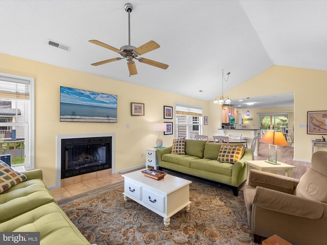 living room featuring vaulted ceiling, a tile fireplace, plenty of natural light, and ceiling fan with notable chandelier