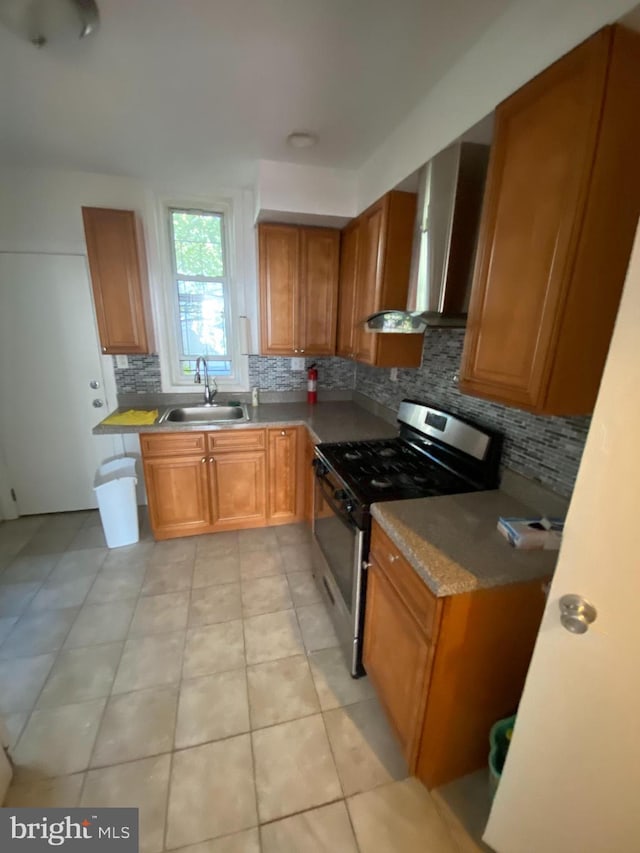 kitchen featuring sink, light tile patterned floors, stainless steel range with gas stovetop, decorative backsplash, and wall chimney range hood